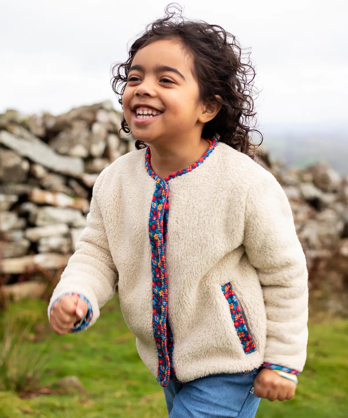 Frugi Juana Fleece jacket in cream with Alpine Blooms corduroy piping, made from recycled polyester, worn by child.