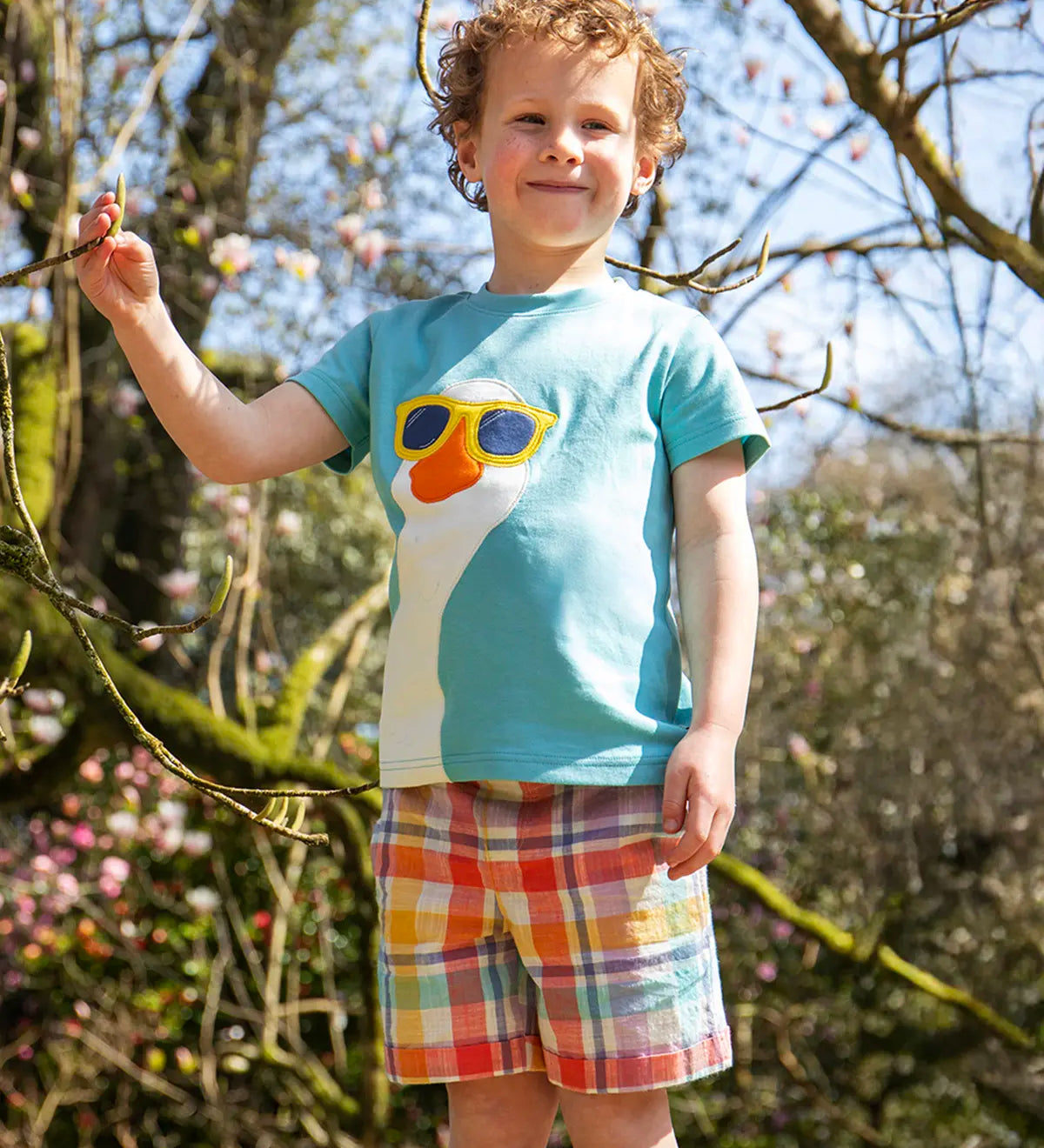 Child wearing Frugi 100% organic cotton Archie slub short in a pastel check design with a blue t-shirt showing trees in the background.