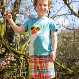 Child wearing Frugi 100% organic cotton Archie slub short in a pastel check design with a blue t-shirt showing trees in the background.