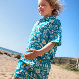 Child wearing Frugi's Kai shorts in blue with repeating beach inspired designs and walking on sand