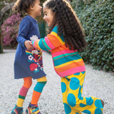 A child wearing Frugi Kari navy rainbow dress and playing with another child wearing the Frugi bight rainbow striped cardigan and super dot trousers available at Babipur.
