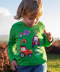 Front of child wearing Frugi's  GOTS organic cotton long sleeve top in green with playful tractor appliques 
