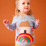 Small child wearing the Frugi's GOTS 100% organic cotton top in light blue showing the cute house on a rainbow applique on the front