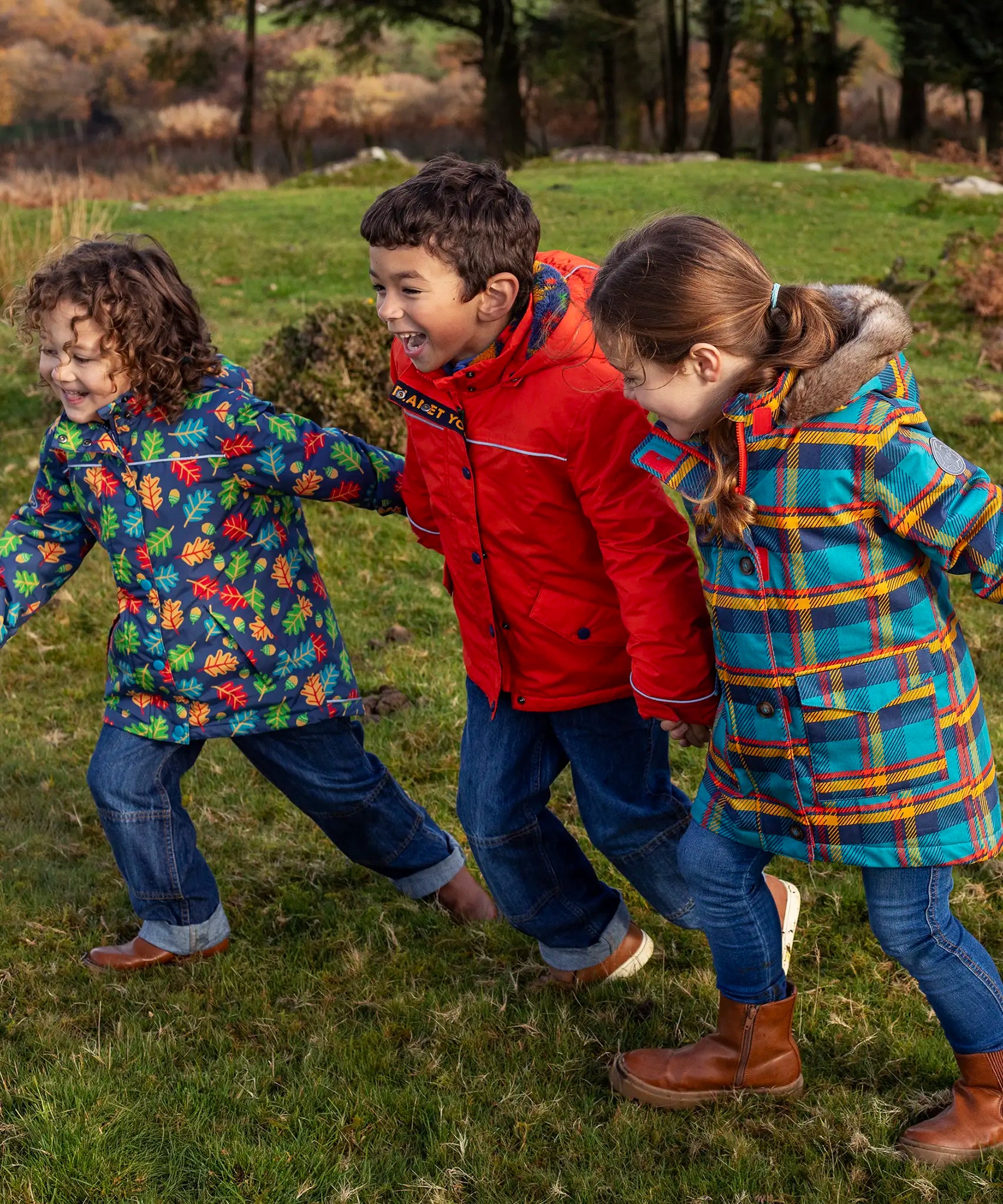 Kids playing on a grassy field and wearing Frugi's playtime, 3 in 1 rambler and a parka coat.