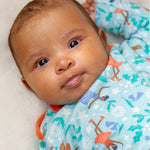A baby lying down and looking forwards is wearing the Frugi Easy Dressing Printed Babygrow - Enchanted Forest. The image shows the ice skating fairies, robin and flower print on a blue fabric