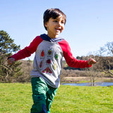 A child running outside on grass and wearing the Frugi compass kids hooded top in grey with red raglan sleeves and navy hood available at Babipur. 