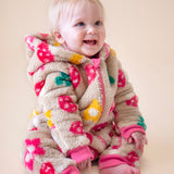A toddler sitting down and wearing the Frugi kids cosy ted snuggle suit in mushroom field available at Babipur. A thick all in one suit in beige with a cute mushroom and flower design
