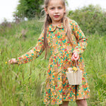 A child outside, holding a wooden basket and wearing the Frugi Autumn Dress - Autumn Friends