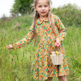 A child outside, holding a wooden basket and wearing the Frugi Autumn Dress - Autumn Friends