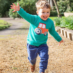 A child playing outside with their arms spread wide, wearing the Frugi Easy On Jumper - Iguana/Tractor