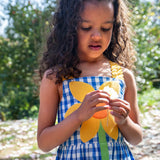 Child wearing Frugi's blue and white check dress with large sunflower patch on the front