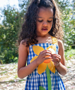 Child wearing Frugi's blue and white check dress with large sunflower patch on the front
