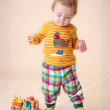 A small child playing with a wooden toy and wearing the Frugi discovery applique top in gold breton/robin and rainbow check bottoms available at Babipur. 