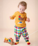 A small child playing with a wooden toy and wearing the Frugi discovery applique top in gold breton/robin and rainbow check bottoms available at Babipur. 