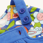A closer look at the adjustable shoulder straps on the Frugi Polly Pinafore Outfit - Blue Tang/Retro Happy. The image also shows the Retro Happy print top, with its smiling planets, flower, cloud, bee and butterfly print.