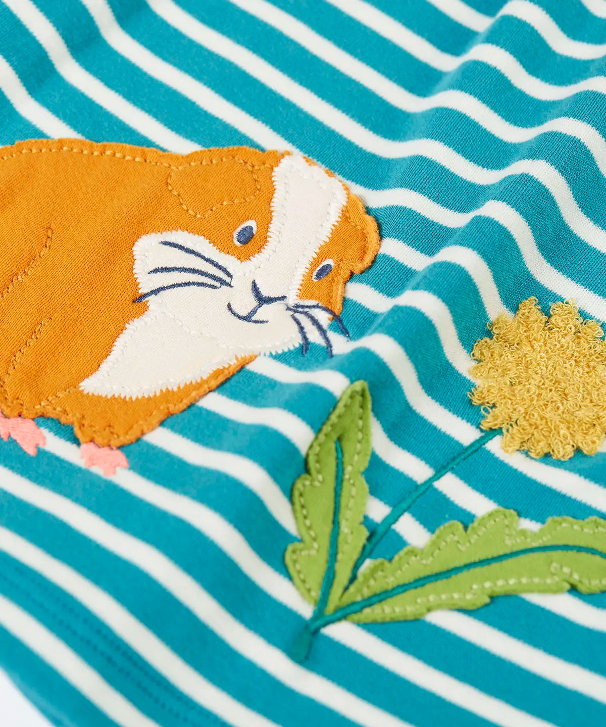 Frugi light blue and white striped kids dress laid flat showing a close up of the guinea pig and flower applique detail on organic cotton fabric
