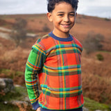 Child wearing Frugi's 100% GOTS organic cotton knitted kids jumper in a traditional tartan design outdoors. Jumper has a relaxed fit