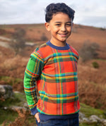 Child wearing Frugi's 100% GOTS organic cotton knitted kids jumper in a traditional tartan design outdoors. Jumper has a relaxed fit