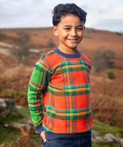 Child wearing Frugi's 100% GOTS organic cotton knitted kids jumper in a traditional tartan design outdoors. Jumper has a relaxed fit
