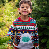A child standing in a forest and wearinf the Frugi forest fairisle/yeti jumper available at Babipur. A GOTS organic cotton jumper with a cute playful yeti on a festive fairisle design. Features a button fasteners on the shoulder