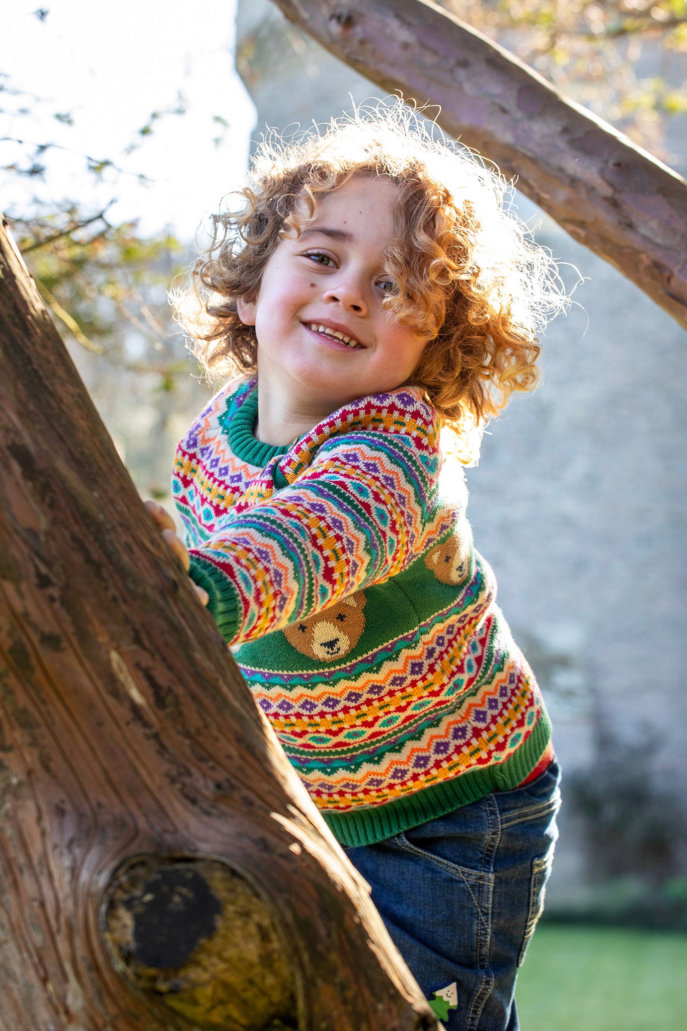 A child playing and wearing the the Frugi fowey fairisle bear knitted jumper available at Babipur. A bright and colourful soft knitted jumper in a fairisle style