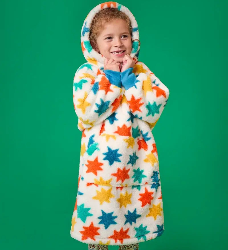 Frugi hooded fleece blanket in cosy cream with blue, orange and yellow star all-over print, worn by girl with hood up.
