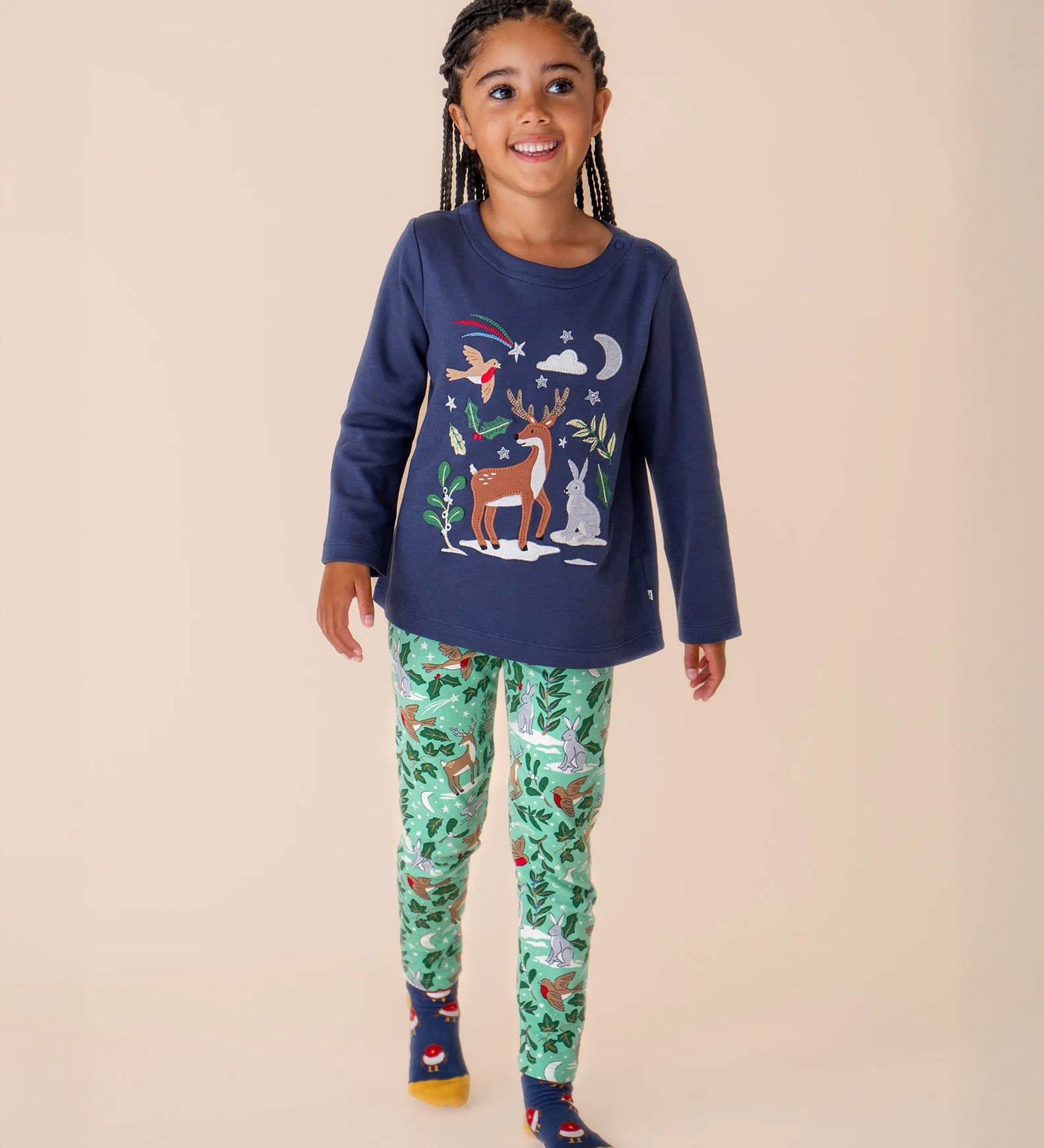 A child wearing the Frugi libby leggings in festive forest with the navy reindeer top as an outfit both available at Babipur. A GOTS organic cotton legging in mint green colour with a winter woodland inspired design.