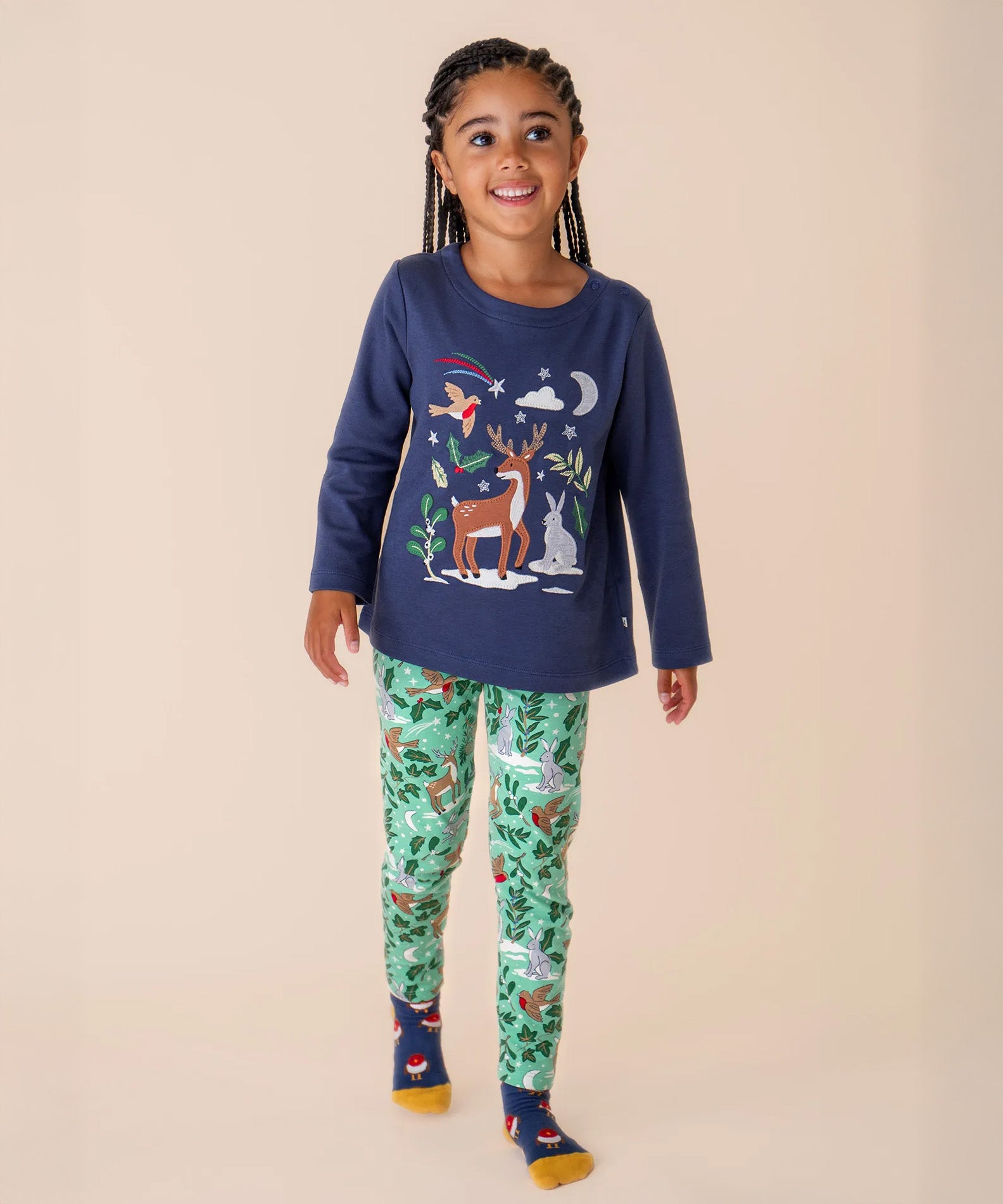A child wearing the Frugi libby leggings in festive forest with the navy reindeer top as an outfit both available at Babipur. A GOTS organic cotton legging in mint green colour with a winter woodland inspired design.