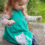 A child outside wearing the Frugi Betty Body - Lingonberry Multi-Stripe underneath a green Frugi cord dress and leggings
