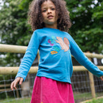 A child outside, wearing the Frugi Adventure Applique Top - Deep Water/Squirrel and a cord Frugi skirt