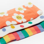 A closer look at the Frugi Rock My Socks - Stay Wild 3 Pack prints. The socks are laid on top of each other with the top sock being the orange and flower print, the middle sock is the white and polka dot print, and the bottom sock is the rainbow stripe print