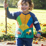 A child playing outside, wearing the Frugi Reva Applique Cardigan - Navy Blue/Sunrise