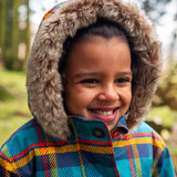 Small child wearing Frugi's Penhale parka coat in a blue red and yellow tartan check with the hood up with fur trim