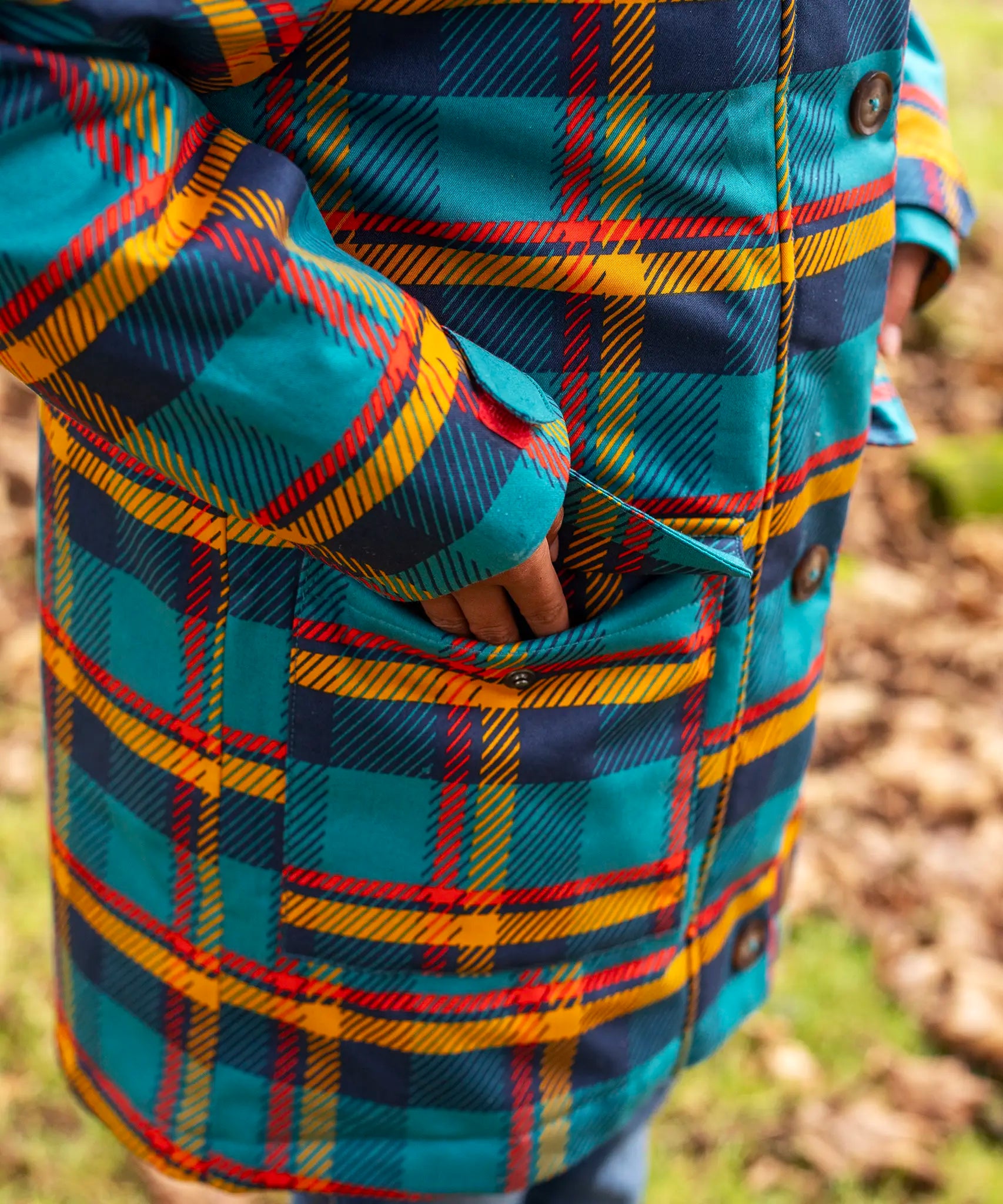 Small child wearing Frugi's Penhale tartan parka coat showing close up of side pocket with popper fastener