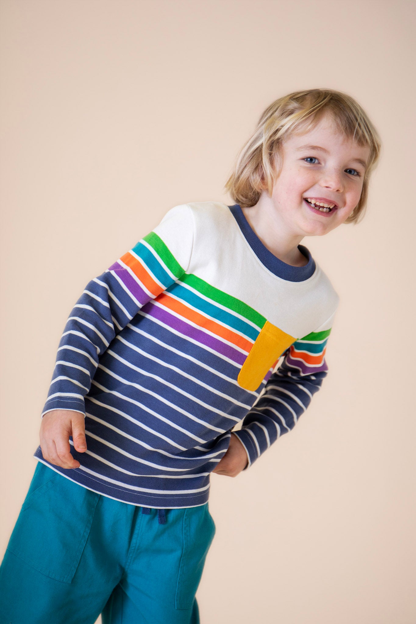 A child wearing the Frugi Piran pocket top in navy stripe available at Babipur. A long sleeve top in a striped design on GOTS organic cotton fabric. Features a yellow chest pocket