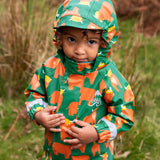 Small child wearing the Frugi waterproof green highland cow puddle buster all in one with the hood up