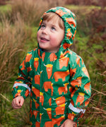 Small child wearing Frugi's waterproof puddle buster coat in highland grazing showing the fitted hood up