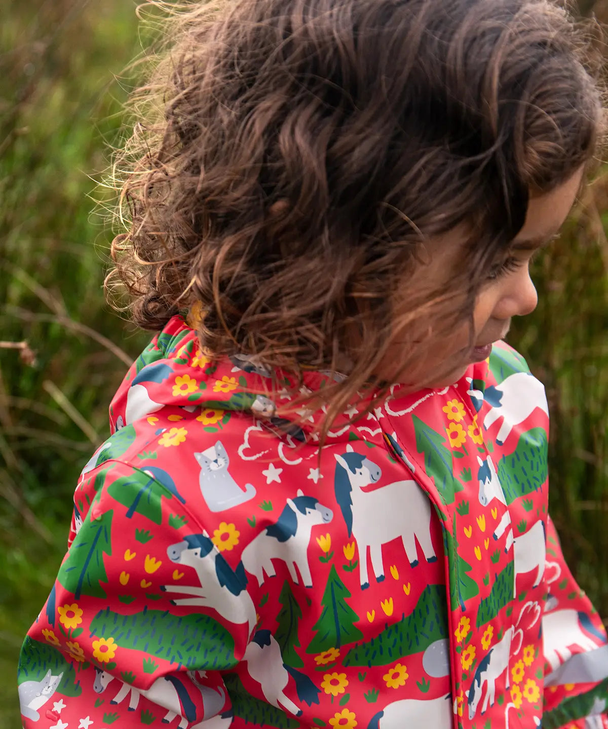 Child wearing the Frugi waterproof puddle buster coat in purrfect ponies showing the repeating cat and pony design inner