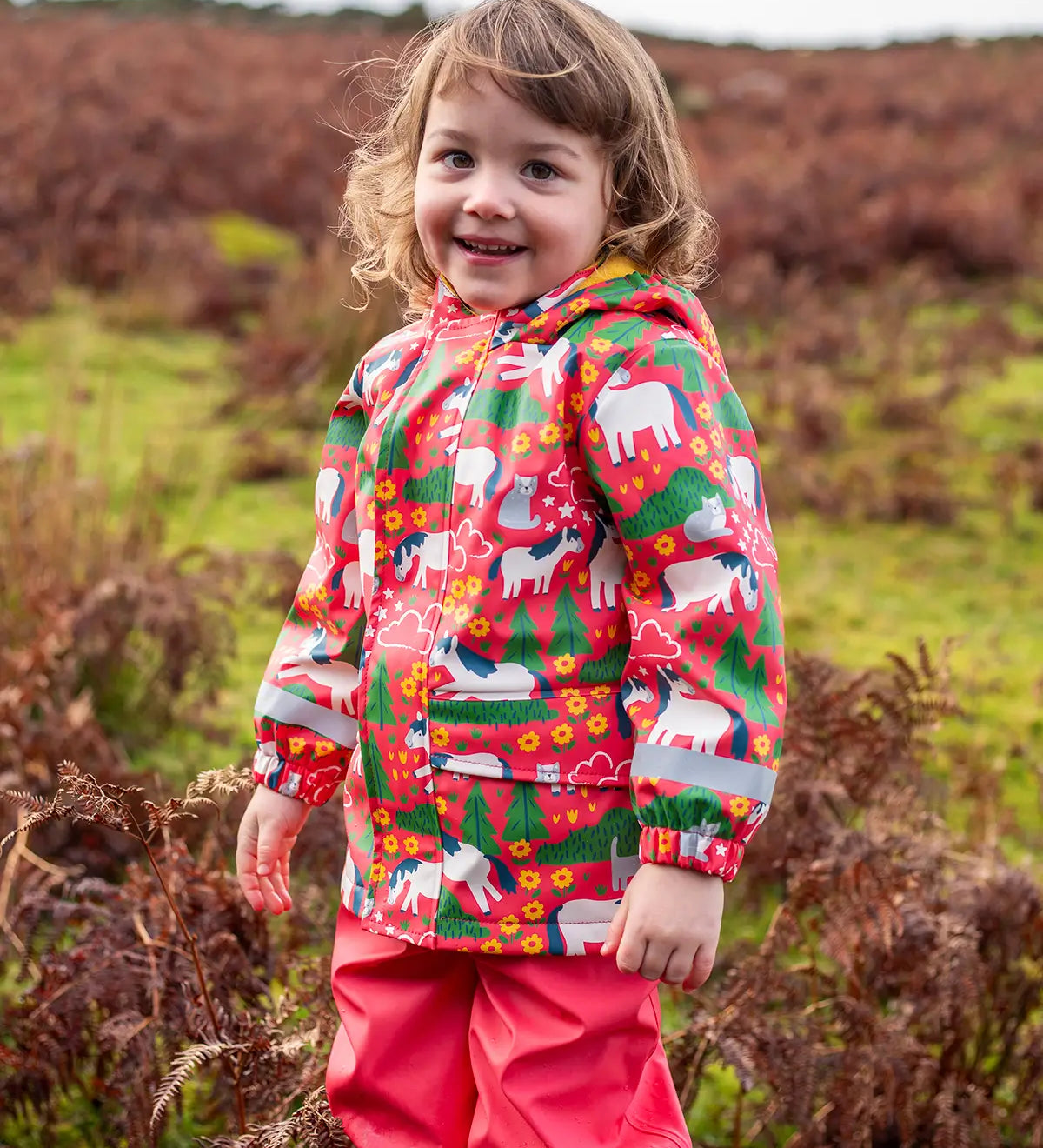 Small child wearing Frugi waterproof puddle buster coat in purrfect ponies showing the side pocket and reflective strip on the cuff