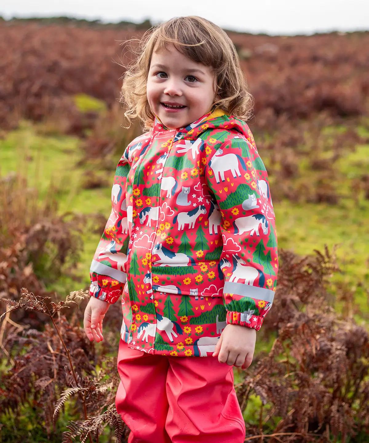 Small child wearing Frugi waterproof puddle buster coat in purrfect ponies showing the side pocket and reflective strip on the cuff