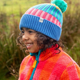 Child wearing the Frugi pastel rainbow striped bobble hat in a grassy field