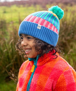 Child wearing the Frugi pastel rainbow striped bobble hat in a grassy field