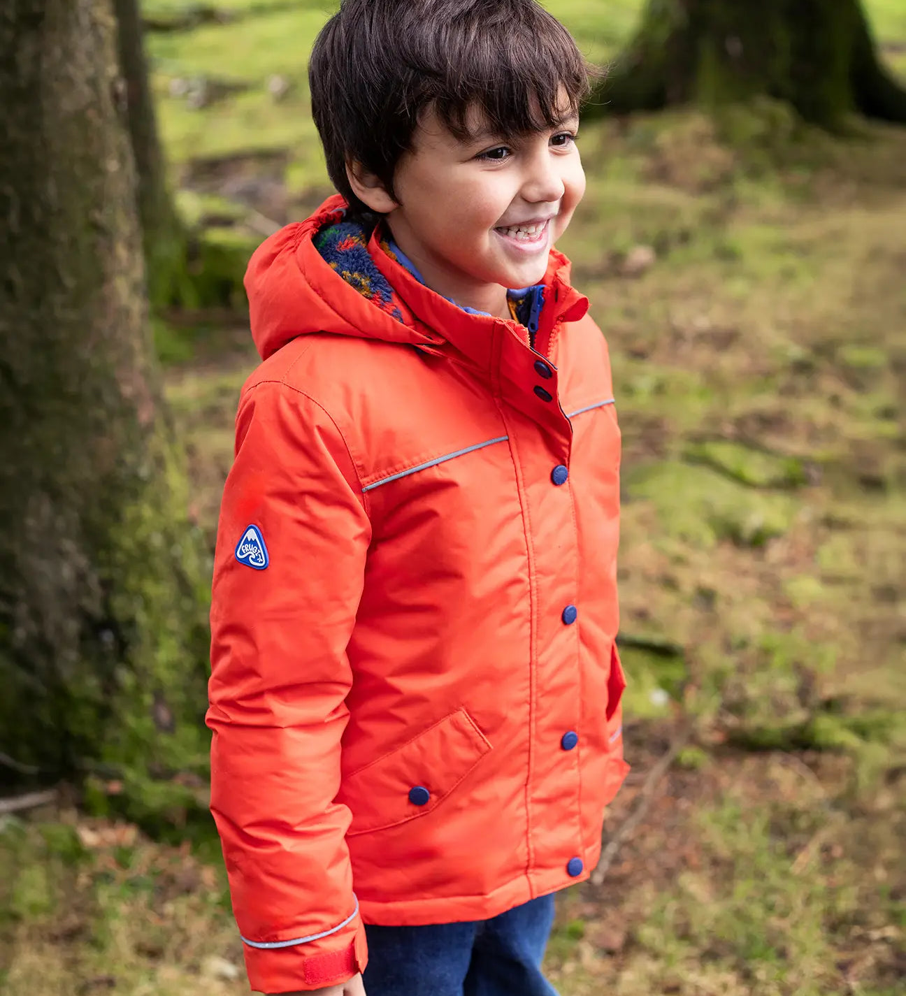 Child wearing the Frugi kids 3 in 1 rambler coat in fire orange upon a star with the hood down