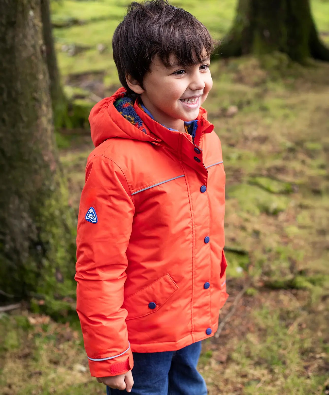 Child wearing the Frugi kids 3 in 1 rambler coat in fire orange upon a star with the hood down