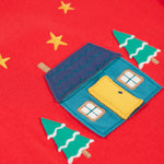 A closer look at the home applique on the Frugi Ira Interactive Applique Top - True Red/Winter Cottage. The house is blue with a navy blue roof, a yellow door and the snowy trees sit either side of the house