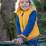 A child sitting on a gate Frugi helston reversible hoodie showing the yellow fleece side available at Babipur