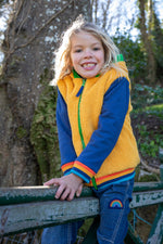 A child sitting on a gate Frugi helston reversible hoodie showing the yellow fleece side available at Babipur