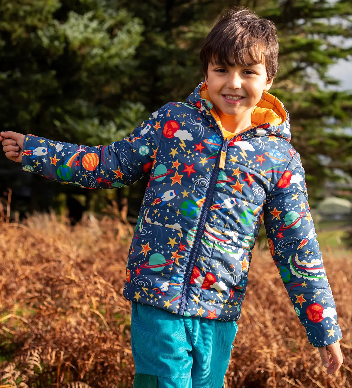 Child wearing the Frugi reversible toasty trail hooded jacket in explore the stars showing the repeating outer space design. 