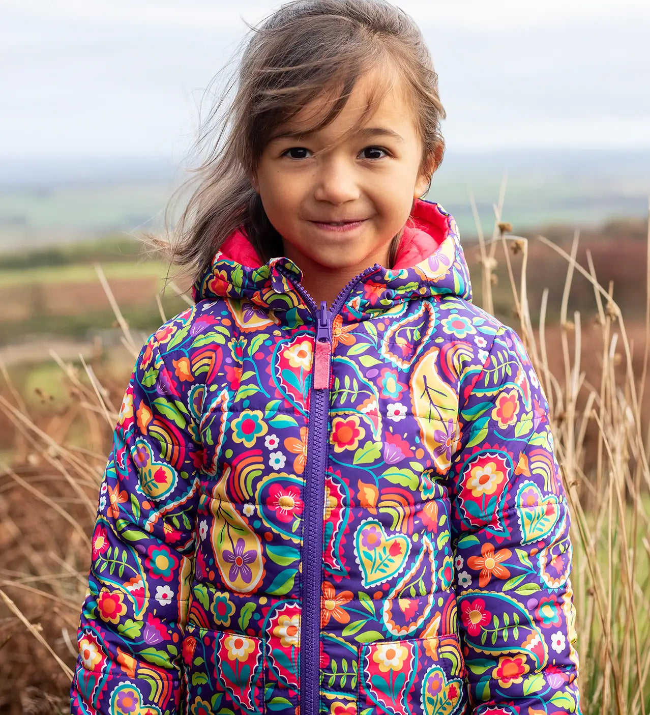 Child wearing the Frugi reversible toasty trail jacket in pretty paisley showing the full front zip and side pockets