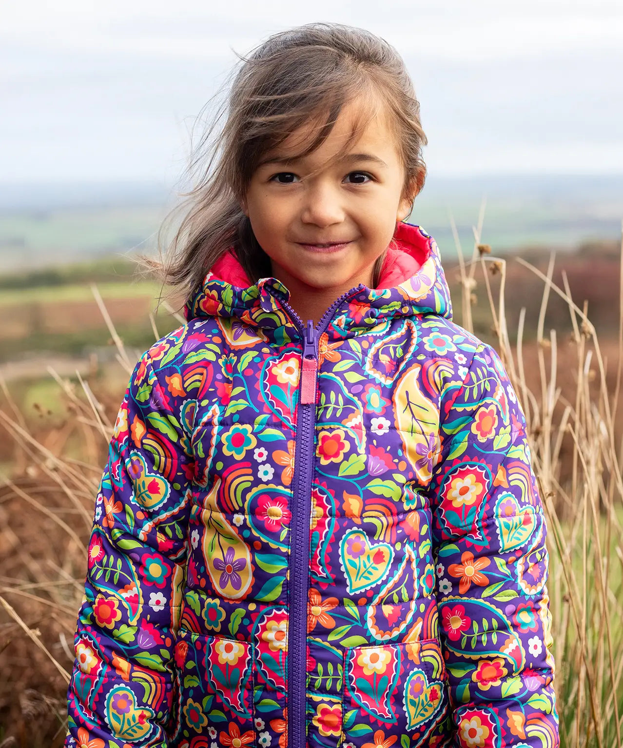 Child wearing the Frugi reversible toasty trail jacket in pretty paisley showing the full front zip and side pockets
